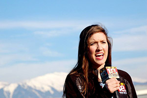 Reporter holding a microphone, standing with a mountain backdrop