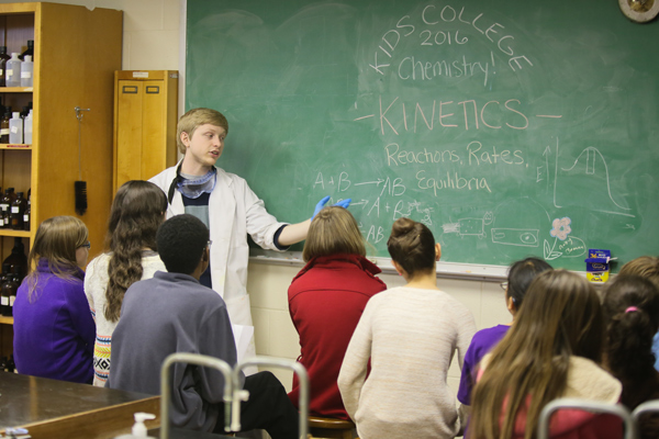 Asbury student at a chalkboard explaining physics concepts to elementary and middle school students