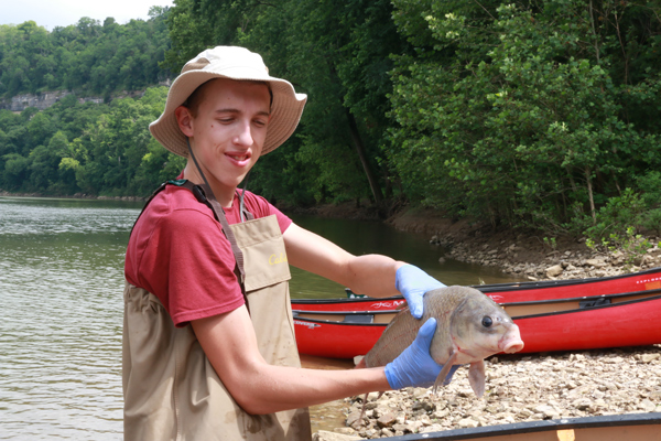 Student in waders holding a fish in his hands