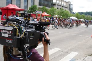 Student holding a TV camera recording a cycling race