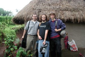 Students posing for a photo in front of a thatched roof hut