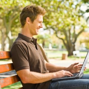 Man with a laptop sitting on a park bench