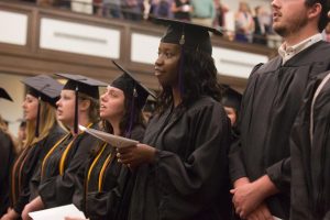 graduate in cap and gown standing in Hughes Auditorium