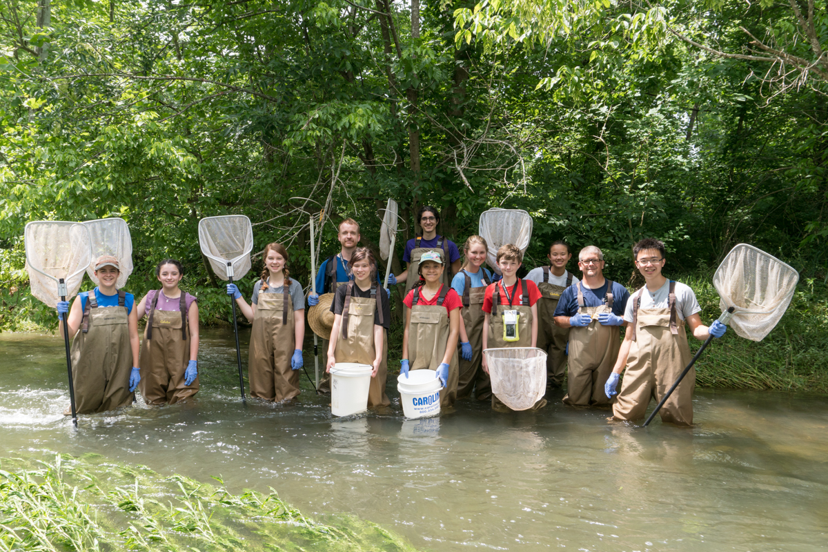 students in waders standing in a creek