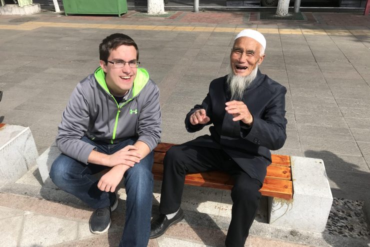 student sitting on a public bench laughing with a Chinese man