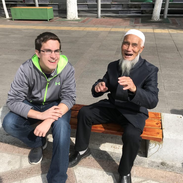 student sitting on a public bench laughing with a Chinese man