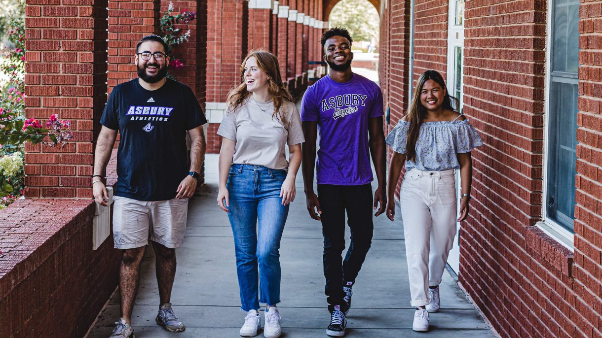 4 Asbury University students smile while walking down a path on campus