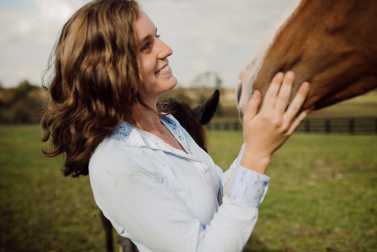 Asbury student smiles and pets a horse in a field