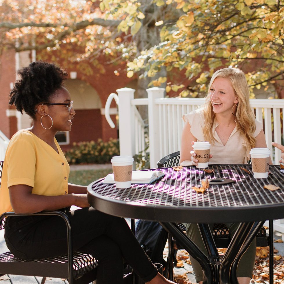 Asbury University students on campus sit at a table cheerfully chatting with friends while coffee cups sit on a table.