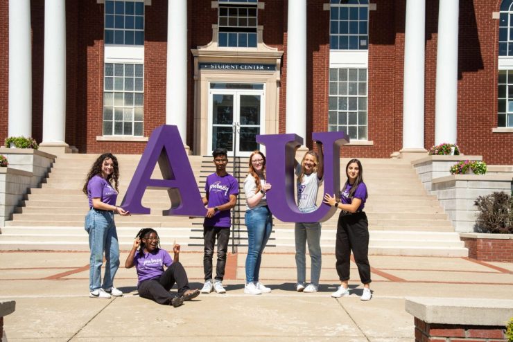 Asbury University students stand in front of the student center holding a large AU sign
