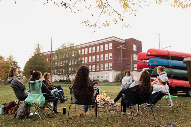 Nine Asbury University students sit around a fire outdoors during the daytime