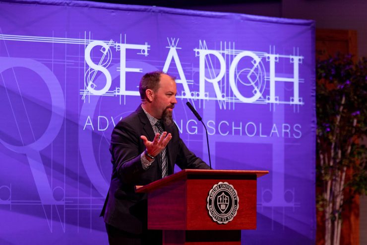 Male speaker behind podium and in front of backdrop at Asbury University's SEARCH Symposium